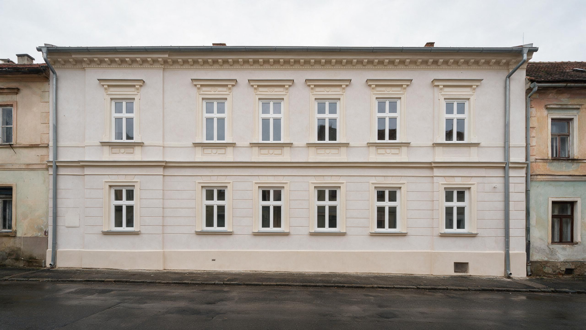 Zrekonstruovaná fasáda historického dvoupodlažního domu s obnovenými šambránami a novými okny